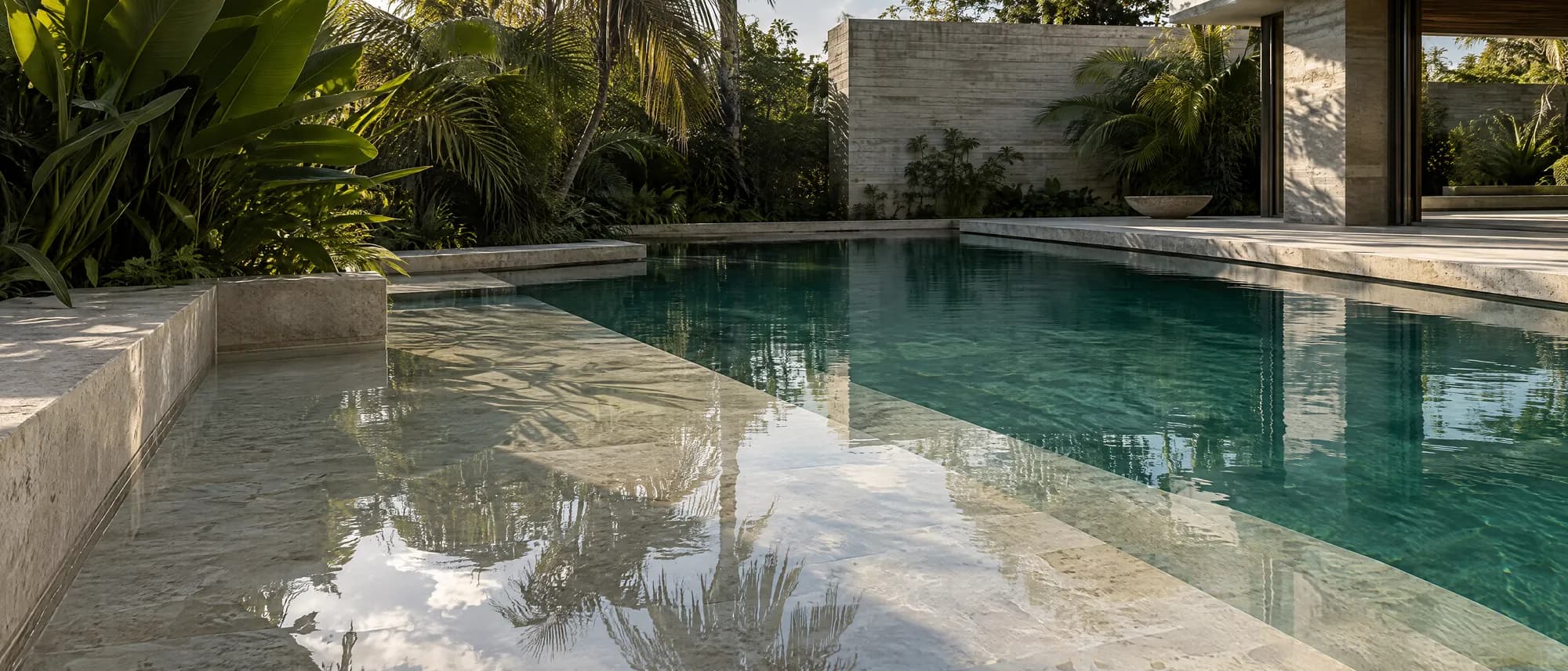 A wide sun shelf under a few inches of water, stepping down into a deep pool beside travertine coping and planting